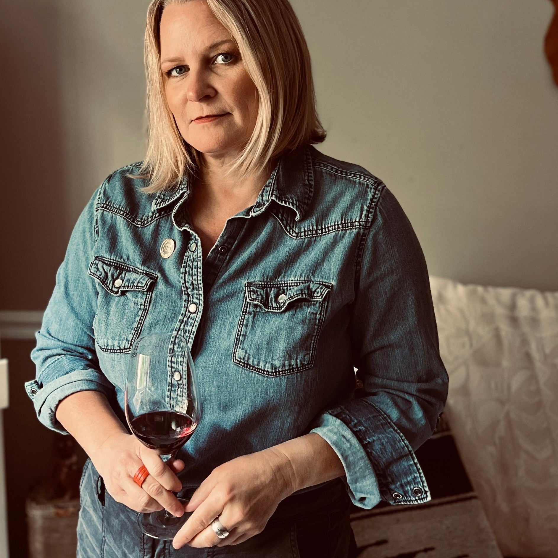 Woman in a denim shirt holding a glass of red wine indoors.