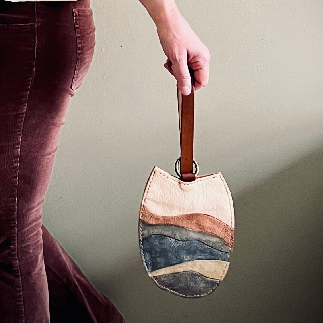 Person holding a handbag with a neutral color palette against a plain background