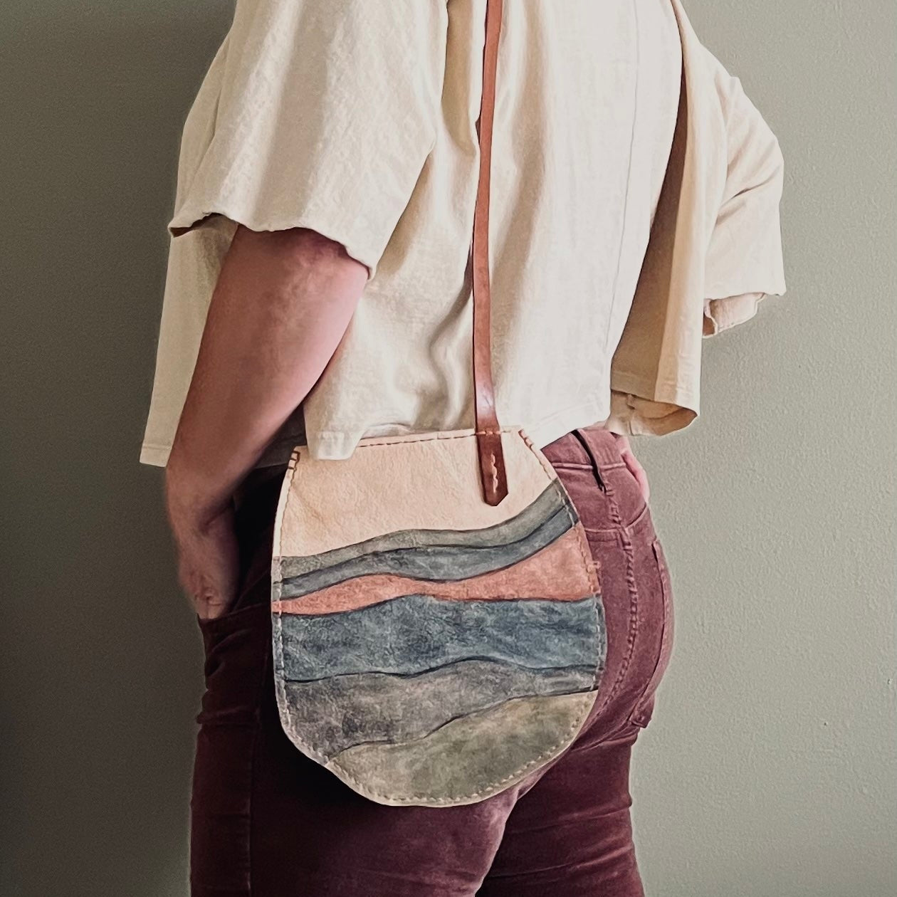 Person wearing a beige shirt and carrying a shoulder bag with a natural leather strap.