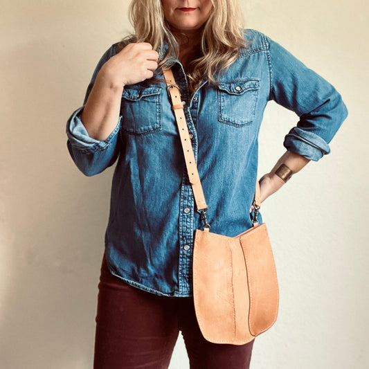 Woman in denim shirt adn burgundy pants wearing a Sondera 1974 Moon River Crossbody bag in natural veg-tan.